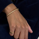 Hand wearing a gold bracelet and ring on a dark background