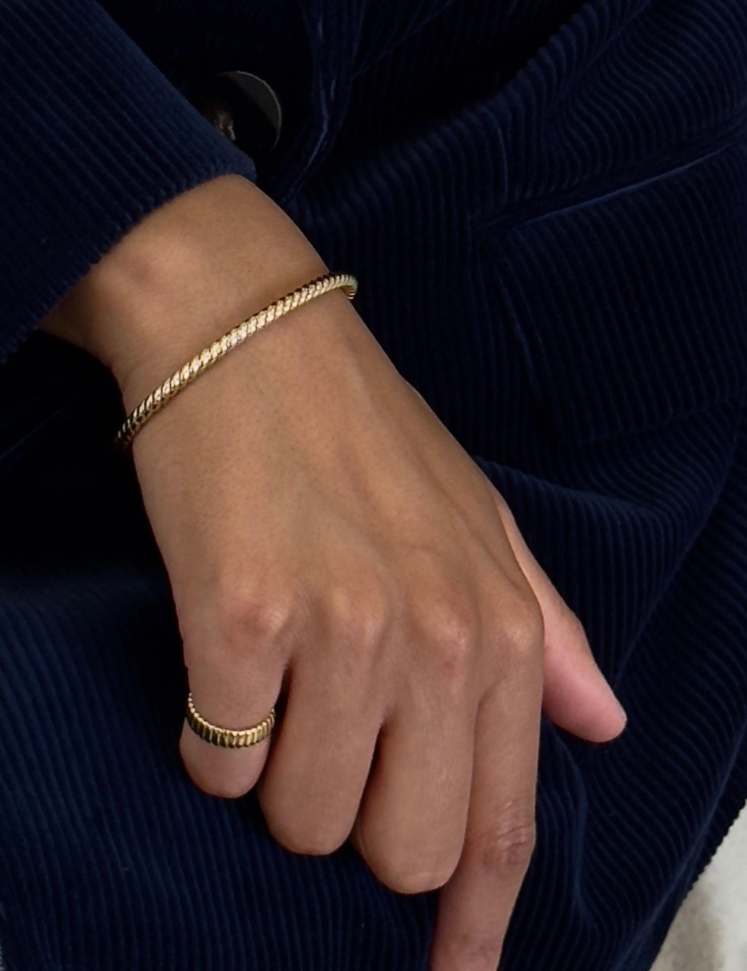 Hand wearing a gold bracelet and ring on a dark background