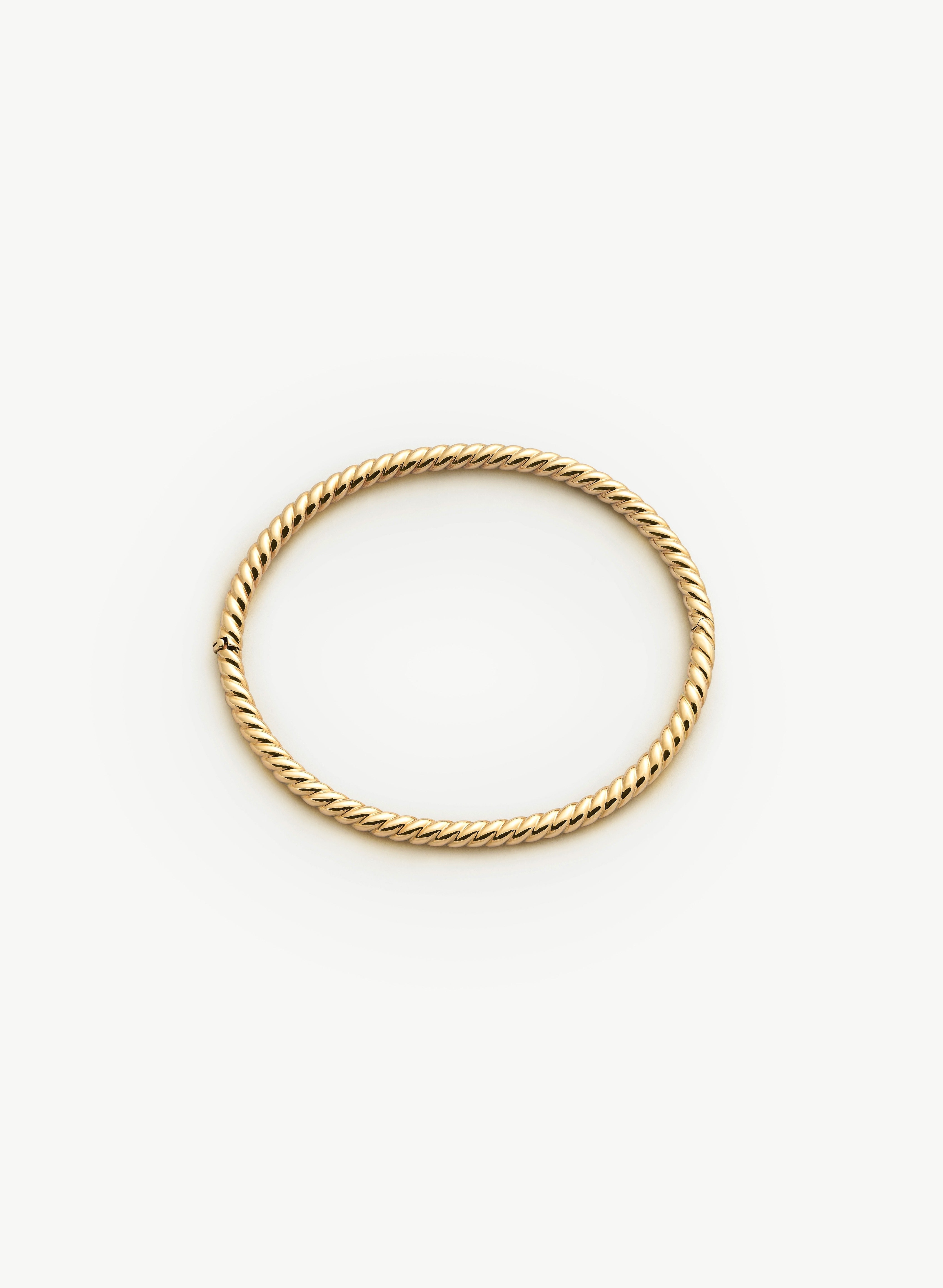 Gold bangle with a twisted design on a white background