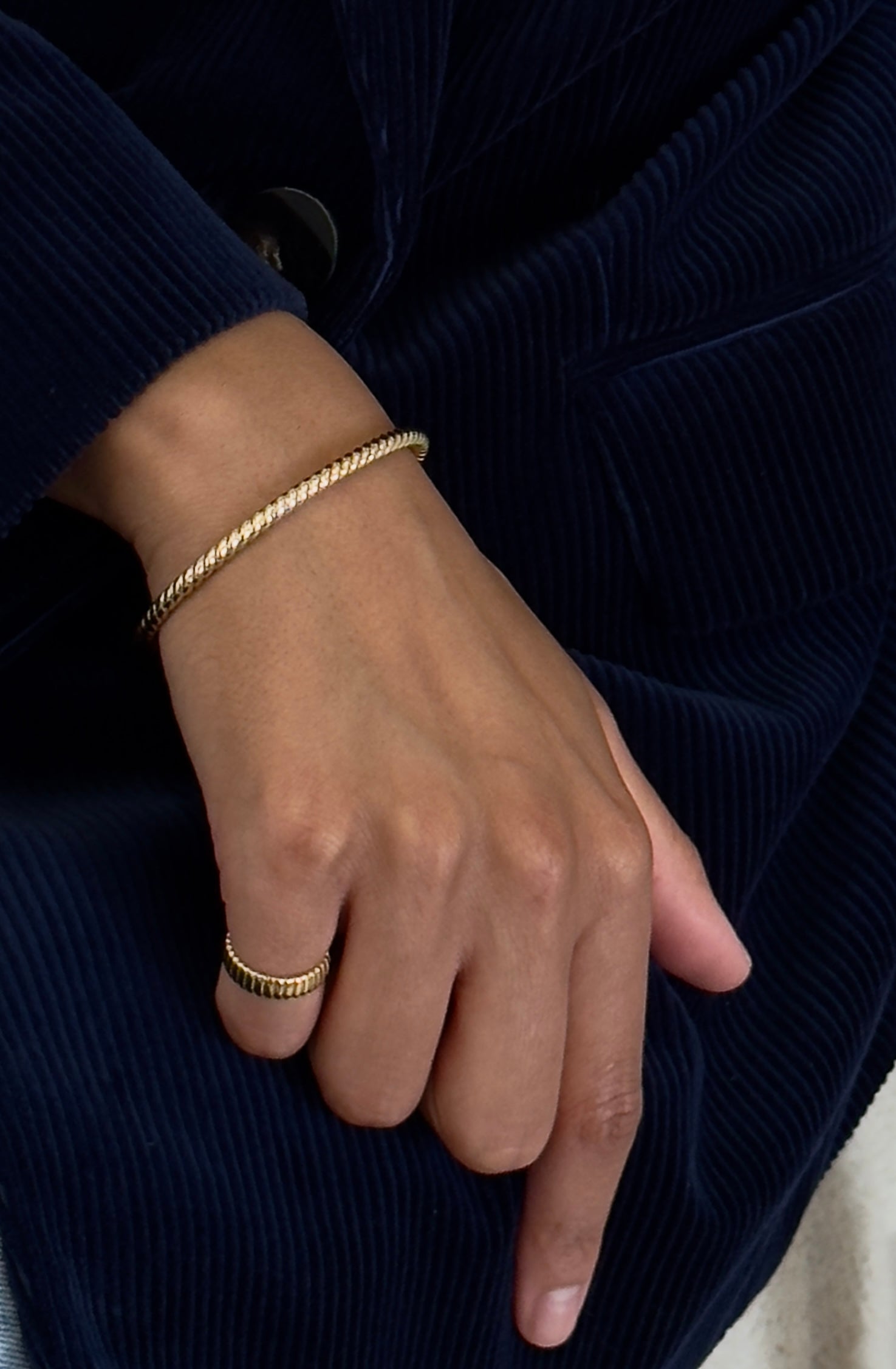 Hand wearing a gold bracelet and ring on a dark background